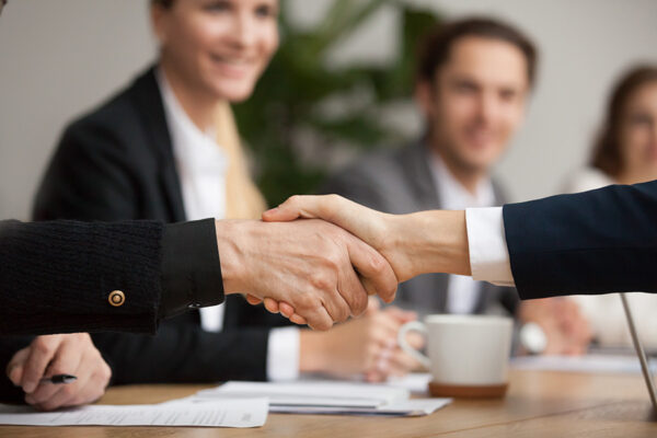 Hands of senior and young businessmen shaking at group meeting, two partners of different age handshaking making agreement or good deal, concluding contract help support concept, close up view.