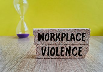 Concept words WORKPLACE VIOLENCE on brick blocks. Beautiful yellow background, hourglass.